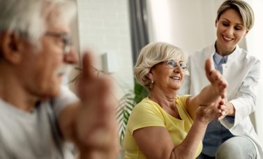 Happy physiotherapist helping to senior couple with stretching e